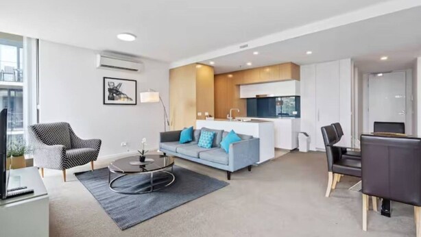 A modern living room with a sofa, a coffee table, and a dining area with chairs. - 2BR Contemporary Comfort in Belconnen (Belconnen)