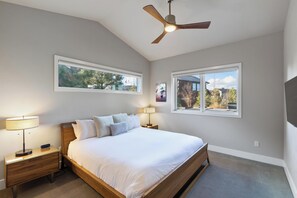 A bedroom with a bed, two bedside tables, a ceiling fan, and two windows.