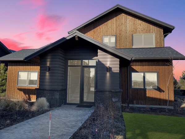 A modern two-story house with a sloped roof, large windows, and a stone foundation.