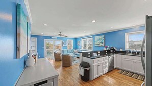 Een moderne keuken met witte kasten, een zwart aanrecht en een zithoek met een blauwe bank.