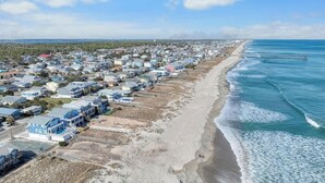 Luchtbeeld van een kustgebied met woonhuizen, een strand en een pier die in de oceaan uitsteekt.