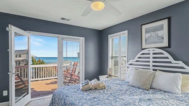 Een slaapkamer met een bed, een plafondventilator en uitzicht op de oceaan door een schuifdeur.