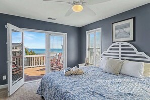 A bedroom with a bed, a ceiling fan, and a view of the ocean through a sliding door. - Sun Sprinkles by Carolina Getaway - Ocean Views, Pool, Walk to Kure Beach (Kure Beach)