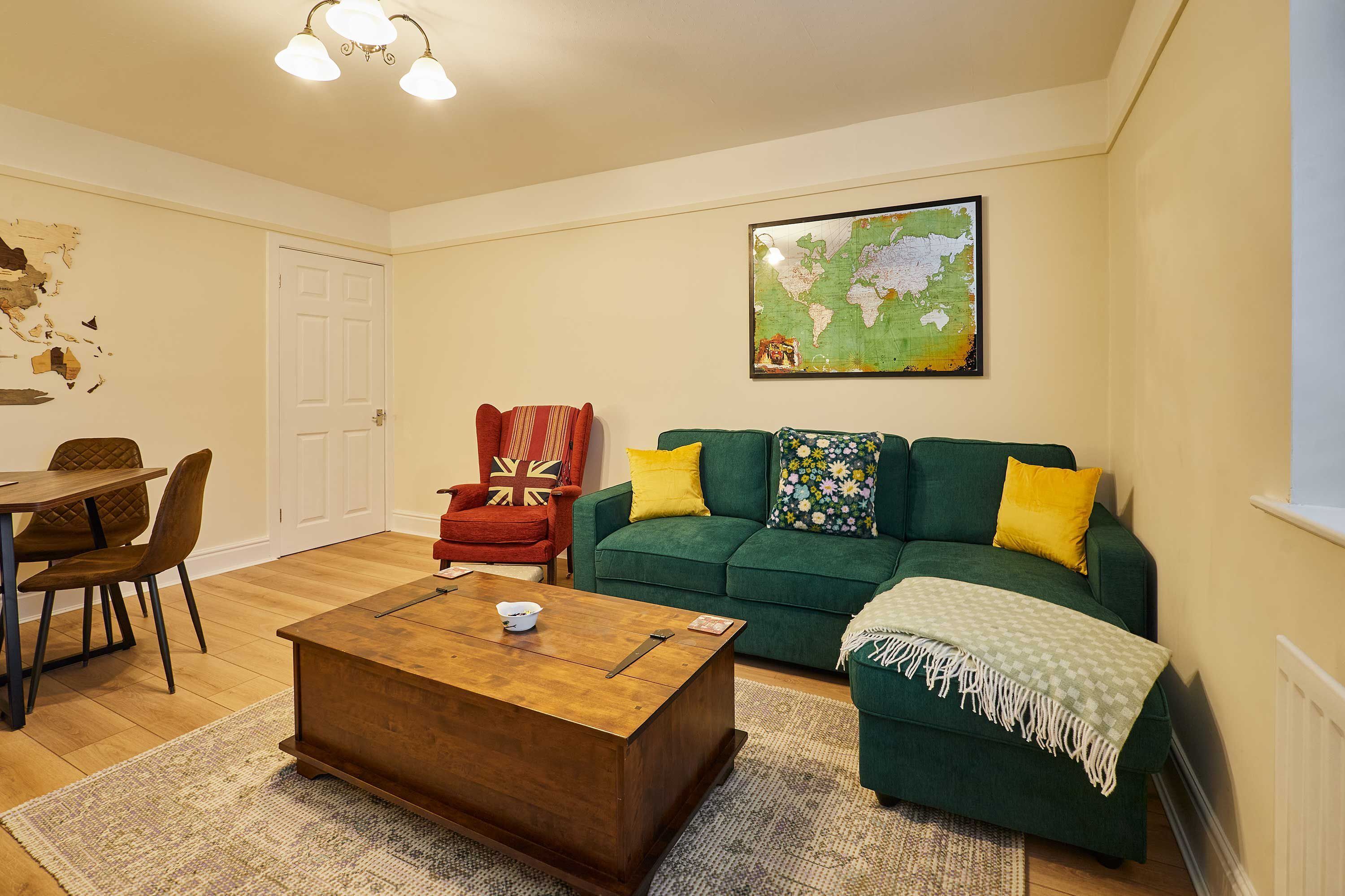 A living room with a wooden coffee table, a green sofa with yellow pillows, a red armchair, and a map on the wall.