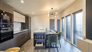 A modern kitchen with built-in appliances, a dining area with a table and chairs, and large windows with blinds. - Host Stay Kingfisher Lodge Amotherby (Malton)