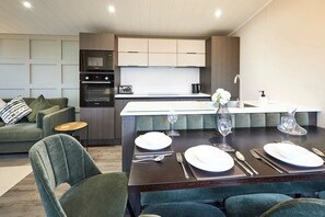 Une cuisine moderne dotée d’appareils électroménagers intégrés, un coin repas avec une table en bois foncé pour quatre personnes, et un canapé vert recouvert de tissu dans le salon.