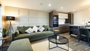 A modern living room with a sectional sofa, a glass coffee table, and a kitchen area with a built-in oven and microwave. - Host Stay Kingfisher Lodge Amotherby (Malton)