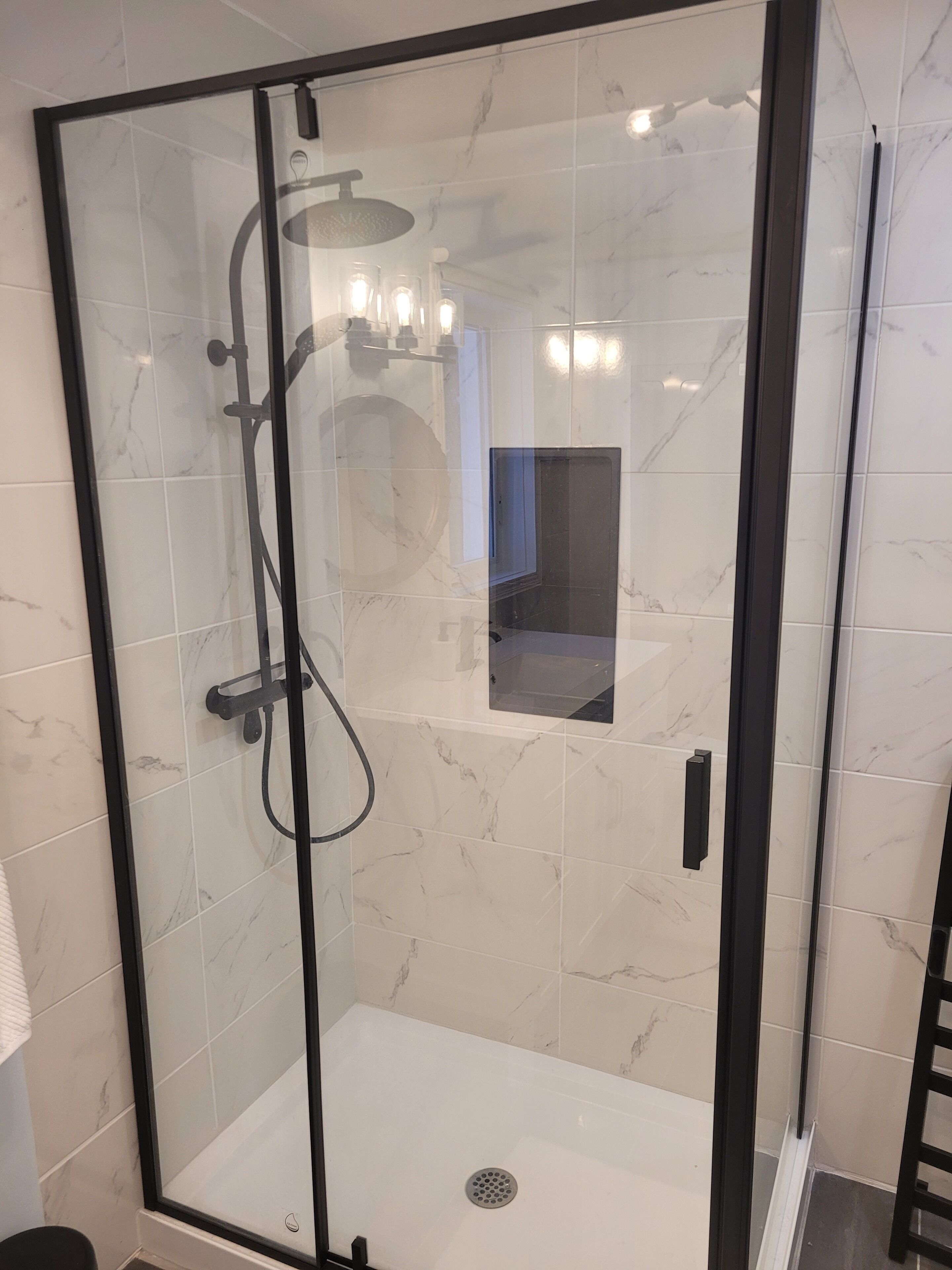 A glass-enclosed shower with a handheld showerhead, a handheld showerhead, and a wall-mounted showerhead.