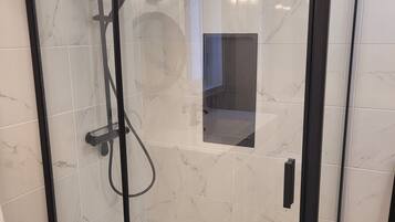 A glass-enclosed shower with a handheld showerhead, a handheld showerhead, and a wall-mounted showerhead.