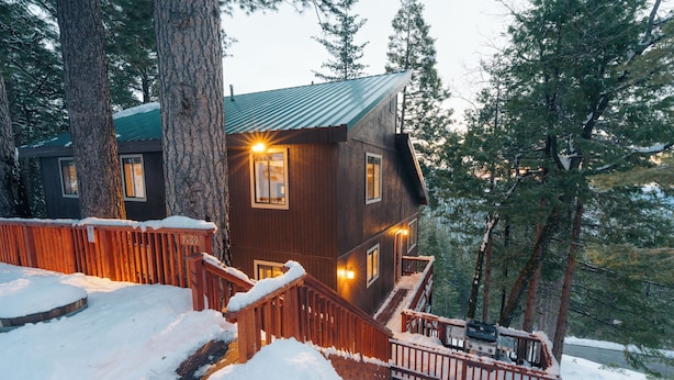 Una cabaña de madera con techo de metal, rodeada de árboles y nieve.
