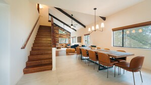 Un interior moderno con una escalera de madera, una zona de comedor con sillas y una mesa, y un ventanal con vistas.