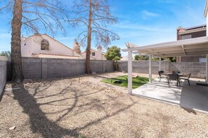 A covered patio with a table and chairs, a small lawn, and a brick wall. - Modern 3BR Home | Pets+7 Min to Airport+Parking (Las Vegas)