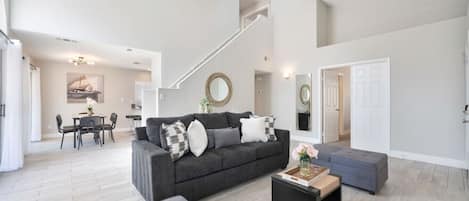 A spacious living area with a grey sofa, a coffee table, and a staircase leading to an upper level.