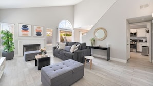 Un salón amplio con chimenea, un conjunto de sofá gris, una mesa de centro y un ventanal con vistas.