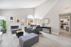 A spacious living room with a fireplace, a grey sofa set, a coffee table, and a large window with a view. - Modern 3BR Home | Pets+7 Min to Airport+Parking (Las Vegas)