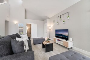 A modern living room with a flat-screen TV, grey sofas, a coffee table, and a TV stand. - Modern 3BR Home | Pets+7 Min to Airport+Parking (Las Vegas)