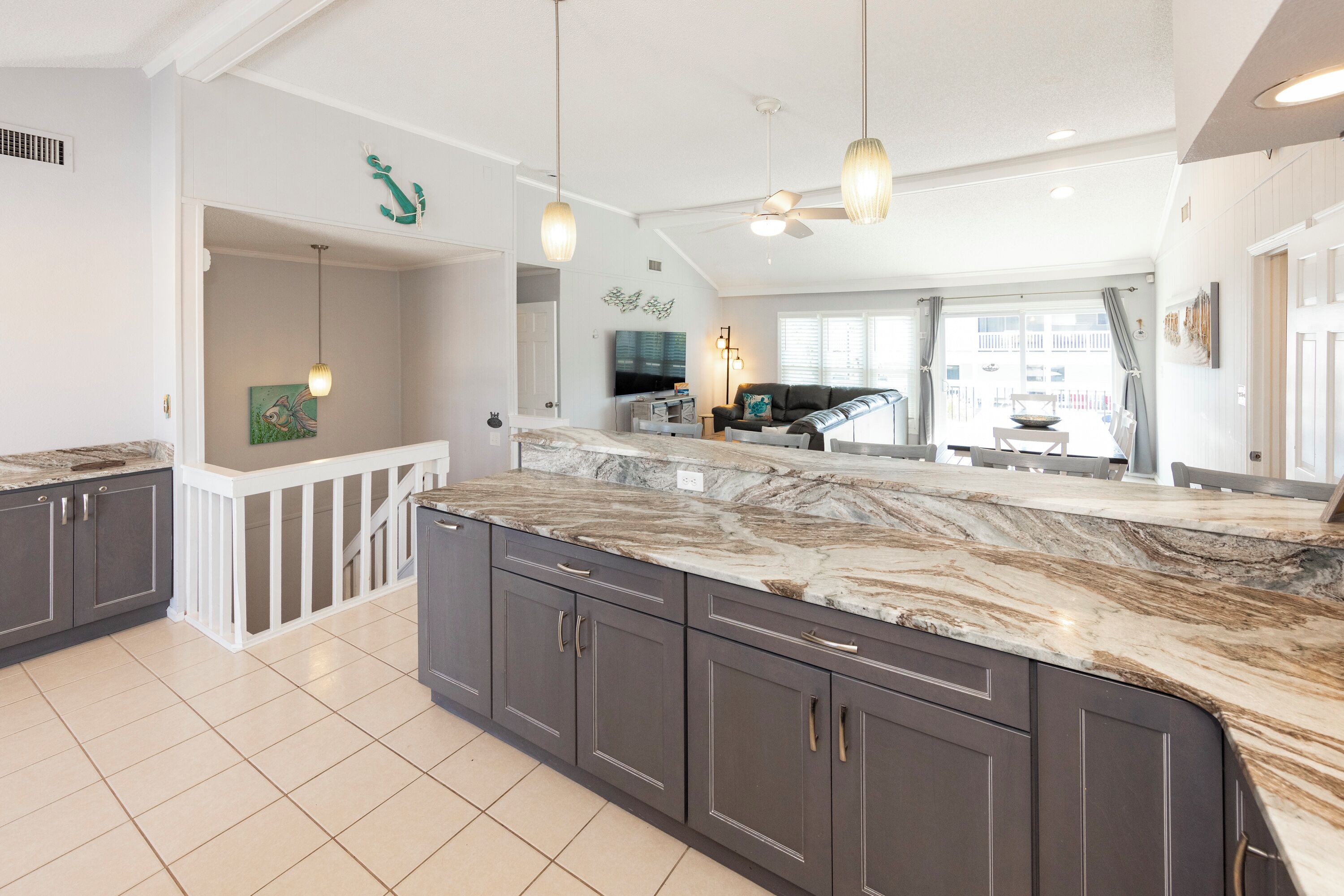 A spacious kitchen with dark cabinets, a marble countertop, pendant lighting, and a view to the dining area.