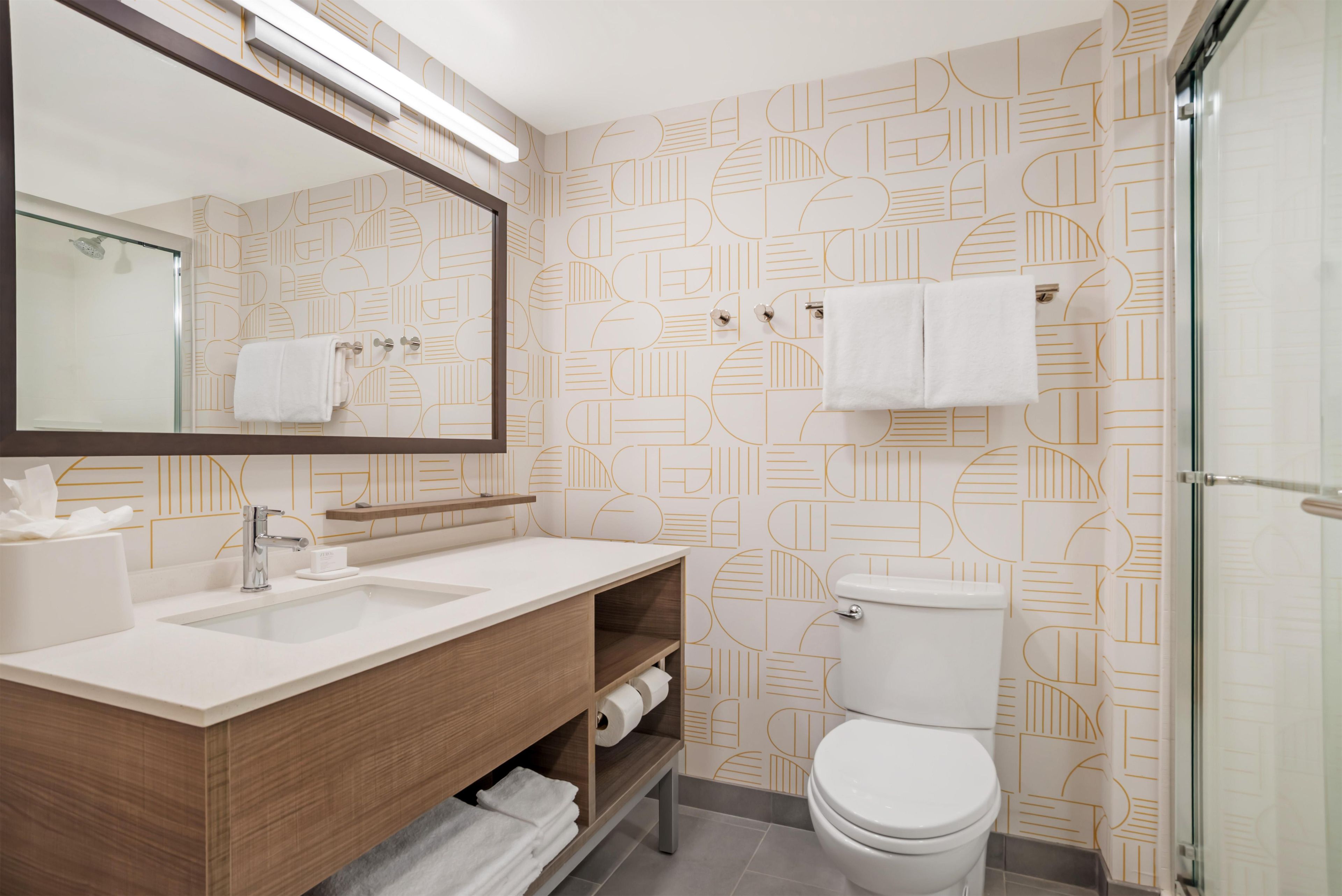 A modern bathroom with a large mirror, two sinks, a toilet, and a shower.