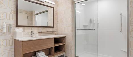 A modern bathroom with a glass shower enclosure, a wooden vanity with a mirror, and patterned wall tiles.