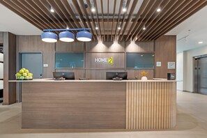 Un comptoir d'accueil moderne, avec une enseigne « HOME 2 », un ordinateur et une petite plante.
