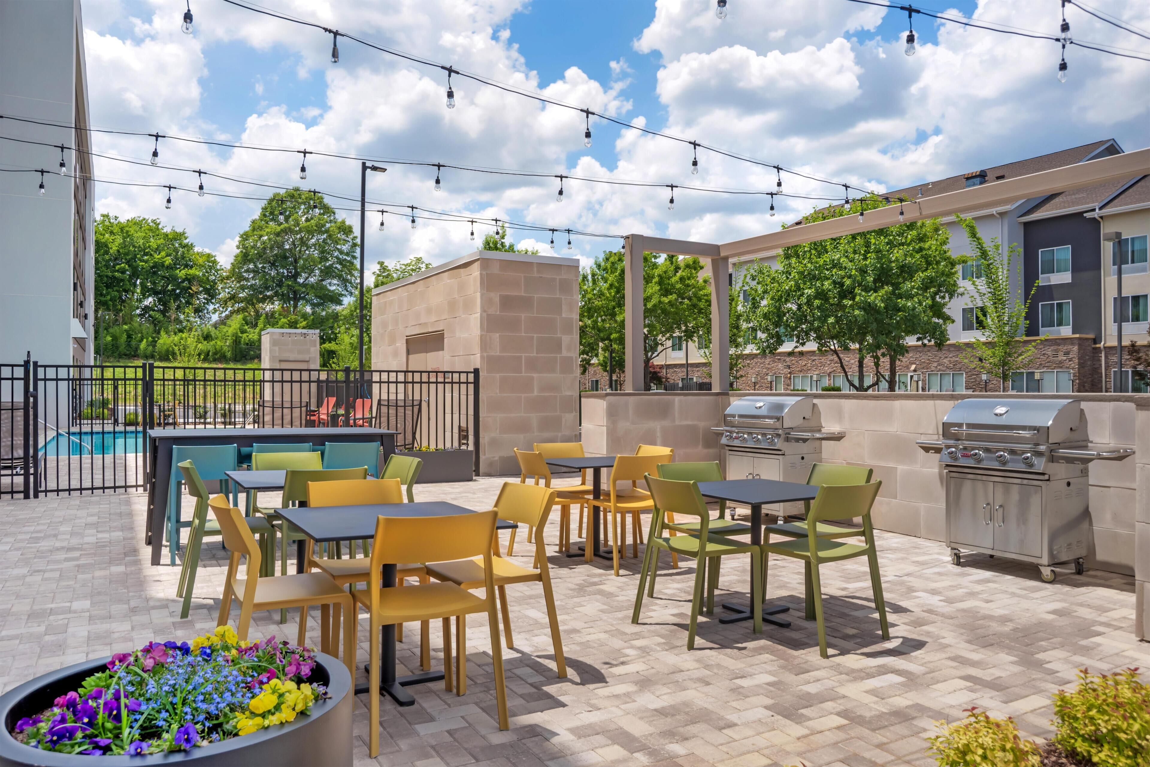 An outdoor patio with tables and chairs, a barbecue grill, and a pool in the background.