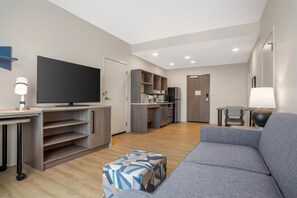 Ein modernes Wohnzimmer mit einem grauen Sofa, einem Flachbildfernseher und einem kleinen Hocker.
