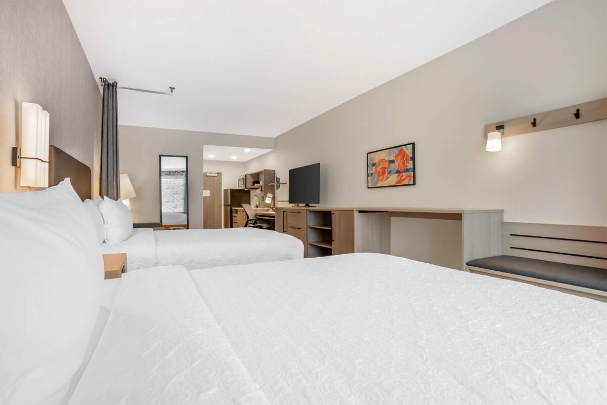 Une chambre d’hôtel avec deux lits, un bureau, une chaise, une télévision et un tableau au mur.
