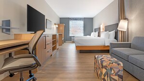 Ein Hotelzimmer mit Bett, Schreibtisch, Stuhl, Sofa, Fernseher und Fenster.