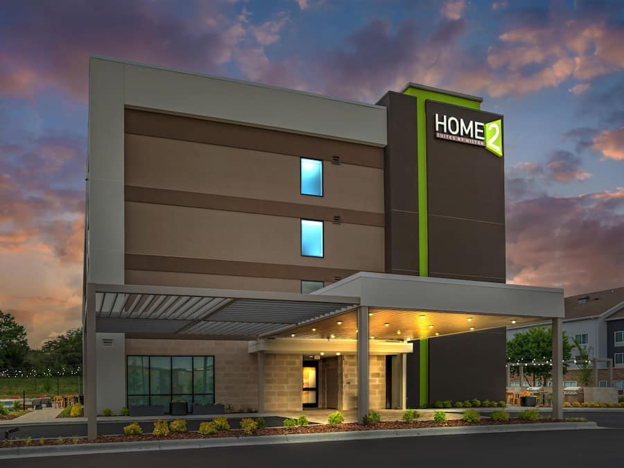A modern hotel with a flat roof, a covered entrance, and a sign reading 'HOME 2 SUITES BY HILTON.'