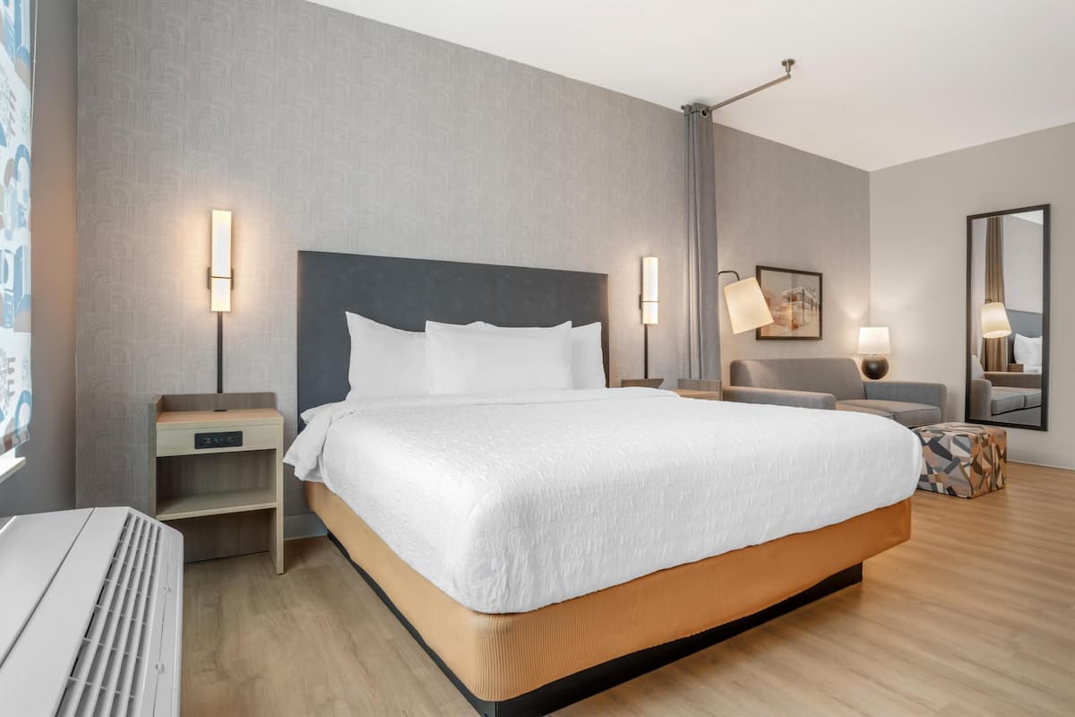 Une chambre d’hôtel avec un grand lit, des tables de chevet, une commode, un miroir et une lampe fixée au mur.