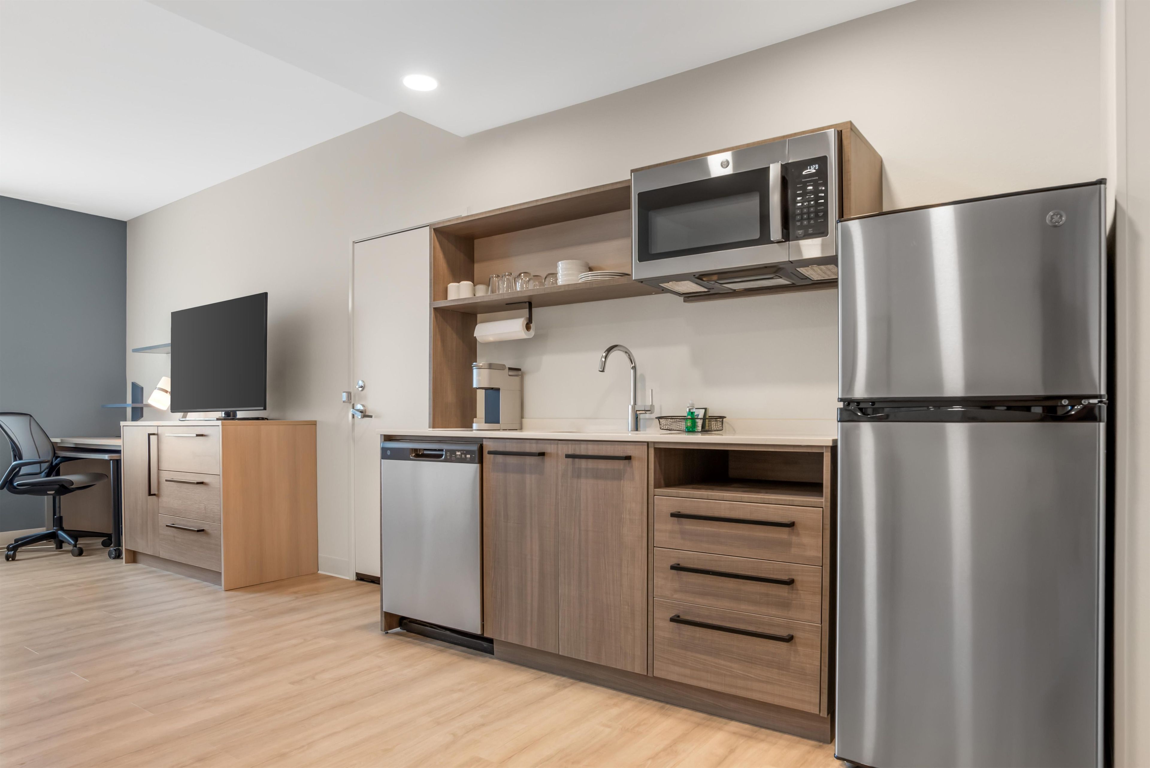 A modern kitchen with a dishwasher, microwave, refrigerator, and wooden cabinets.