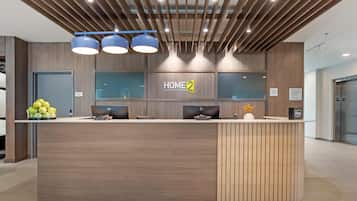 A modern hotel reception desk with a 'HOME 2' sign, a computer, and a small plant.