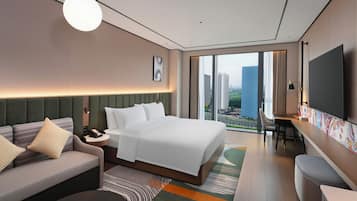A modern hotel room with a large bed, a sofa, a desk, and a TV.