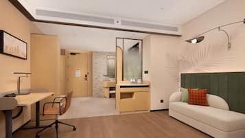 A modern hotel room with a desk, chair, sofa, and a large mirror.