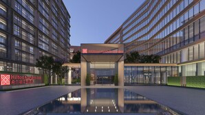 Moderne hotelentree met een reflecterend zwembad, glazen gevel en borden met Hilton Garden Inn.