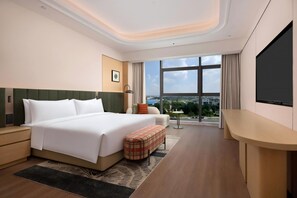 A hotel room with a large bed, a desk, a chair, a small table, and a view of the city through large windows. - Hilton Garden Inn Chengdu Shuangliu International Airport (Chengdu)