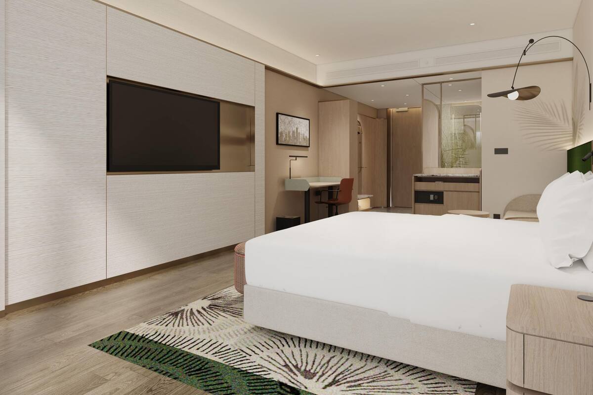 Une chambre d’hôtel moderne dotée d’un grand lit, d’un téléviseur à écran plat fixé au mur, d’un bureau avec une chaise, d’un miroir et d’une petite salle de bain.
