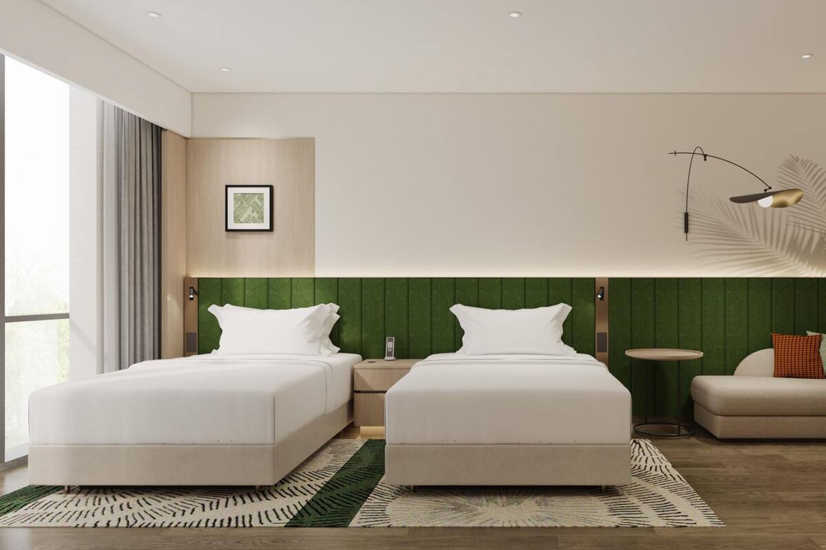 Une chambre d’hôtel moderne avec deux lits, un mur d’accent vert, une petite table ronde et un canapé.