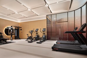 Une salle de sport moderne équipée de machines de cardio, de poids et d’un grand miroir.