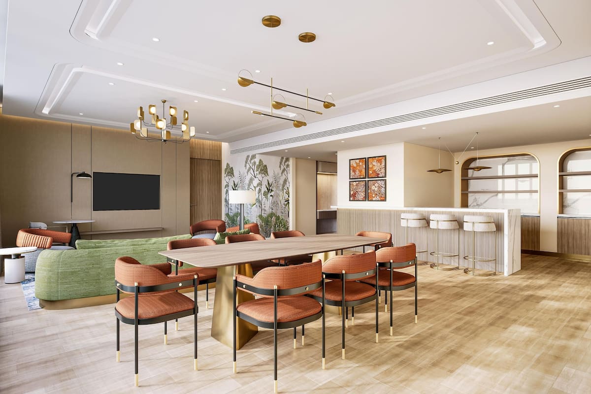 A modern hotel room with a dining area, a flat-screen TV, a green sofa, and a large wooden table with chairs.