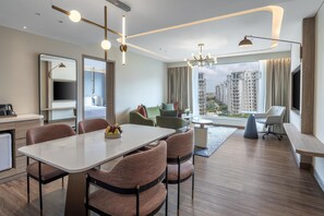 A modern hotel room with a dining area, a seating area with a view, and a large window overlooking a cityscape.