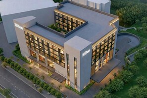 A modern hotel with a flat roof, large windows, and a landscaped garden. - Hilton Lucknow Gomti Nagar (Lucknow)