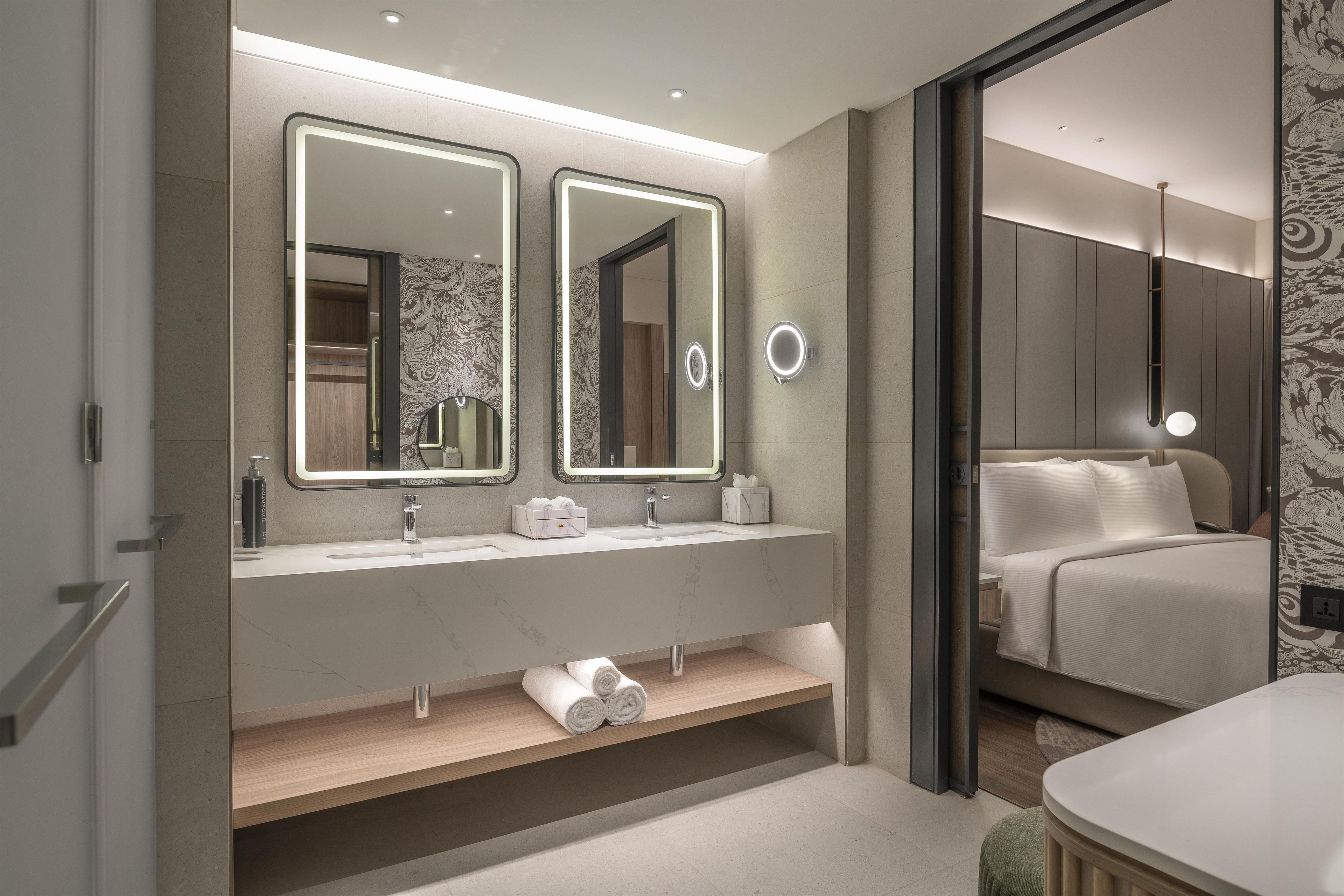 A modern bathroom with a double vanity, two mirrors, a towel rack, and a toilet.