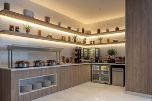 A modern kitchen with built-in appliances, a refrigerated display case, and a variety of decorative items on shelves. - Hilton Lucknow Gomti Nagar (Lucknow)