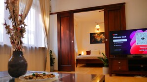 A hotel room with a bed, a TV displaying a welcome screen, a vase with flowers, and a dining table with a plate of food. - Serene 1-bedroom apartment in the heart of Warszawa (Warszawa)