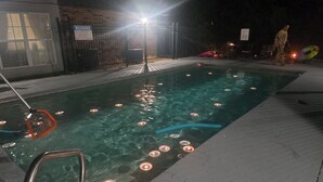 A swimming pool with lights, a metal ladder, and a warning sign on a brick wall.