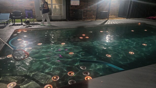 A swimming pool with clear water, surrounded by a brick wall, and a warning sign on the gate.