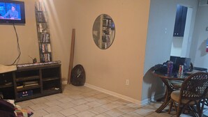 A living room with a television, bookshelf, clock, and a bench.