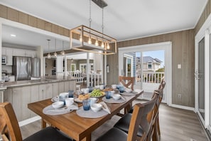 Une cuisine moderne dotée d’un îlot central, d’un coin repas avec une table et des chaises en bois, et offrant une vue sur un quartier résidentiel.