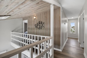 A modern interior with a wooden ceiling, a white railing, and a hallway leading to a door with a view.